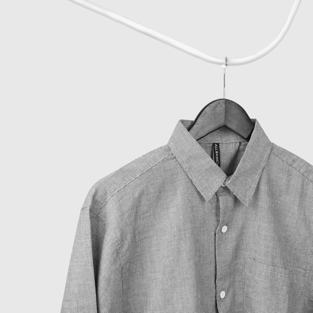 Close-up of a gray button-up shirt hanging on a wire hanger against a white wall.