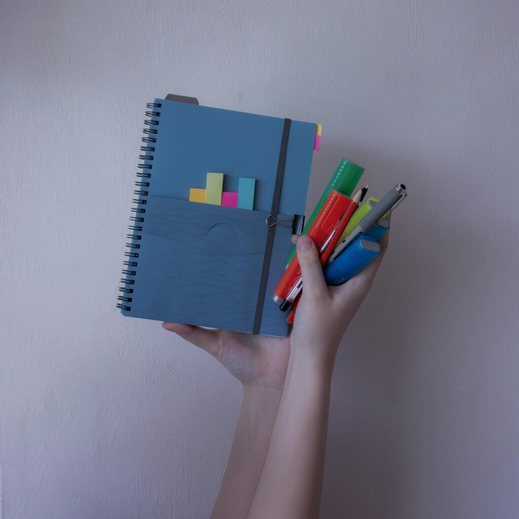 A person holding a notebook with colorful pens and sticky notes, showcasing stationery organization.